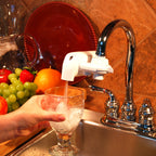 Person pouring water from a F8 White faucet into a glass with ice cubes, surrounded by fruits and kitchen items.