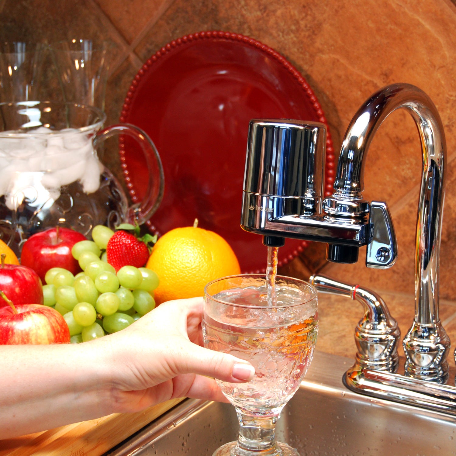 Person filling a glass with water from a faucet-mounted filter in a kitchen.